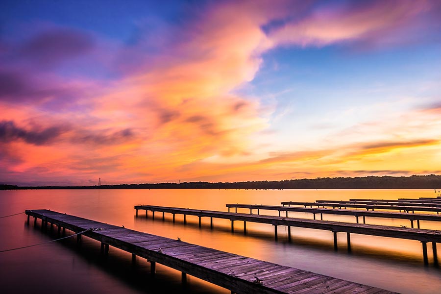 Fulton, MS Insurance - Small Lake With Wooden Docks at Sunset, Sky Full of Vibrant Colors Reflecting off the Water