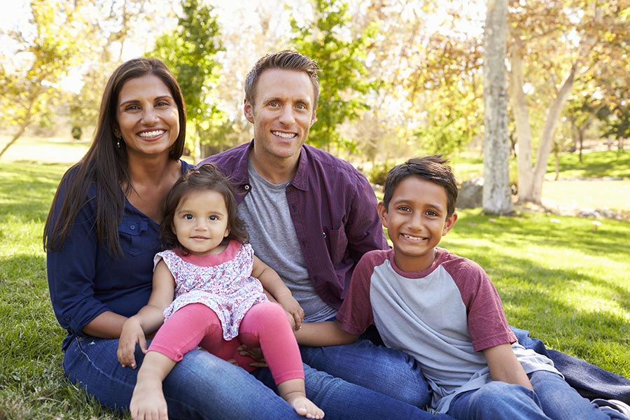 Personal Insurance - Young Family Sitting on a Grassy Field Smiling Together
